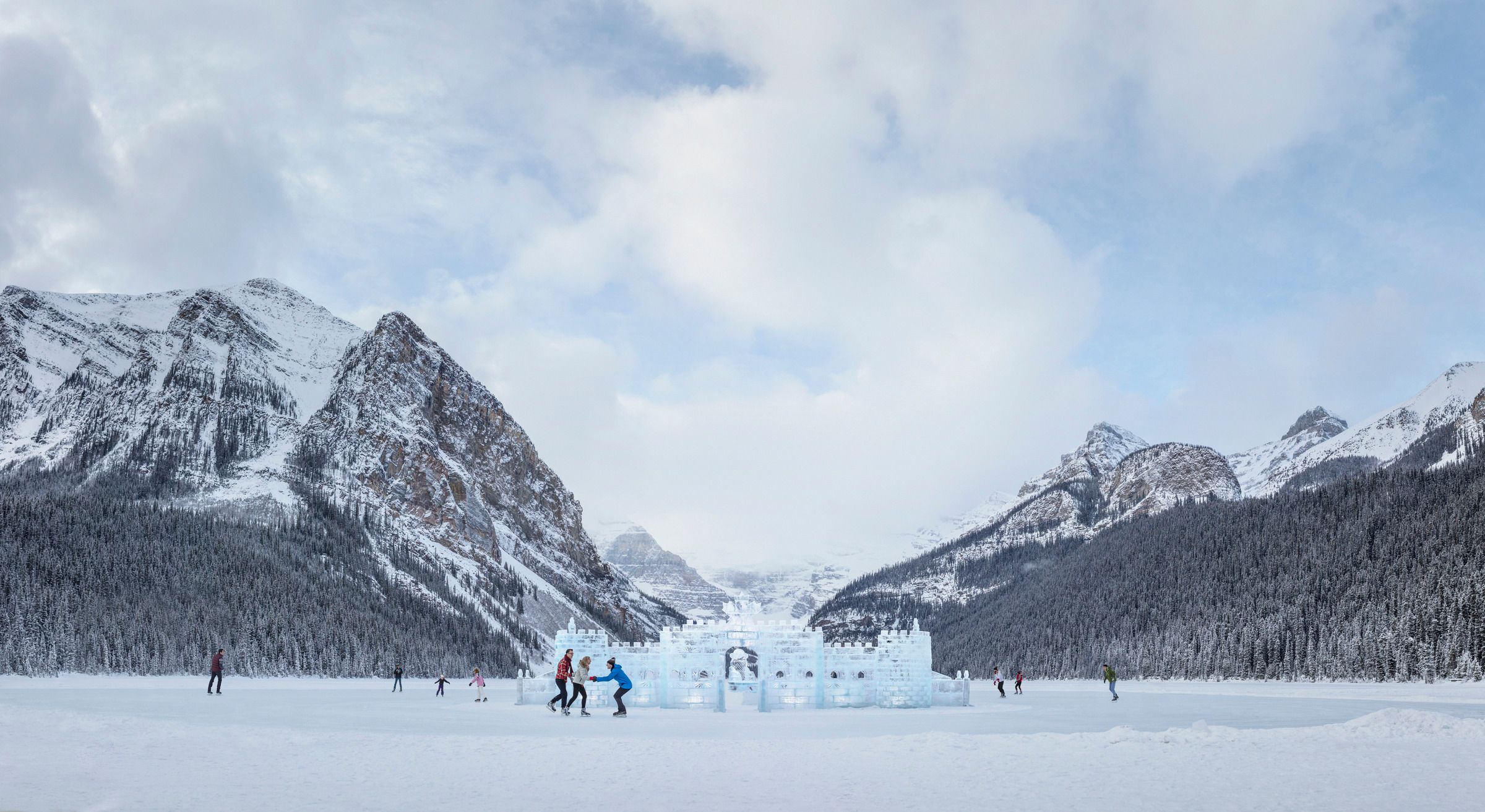 People ice skating around an ice castle, mountains in the background, on Lake Louise in Banff National Park.