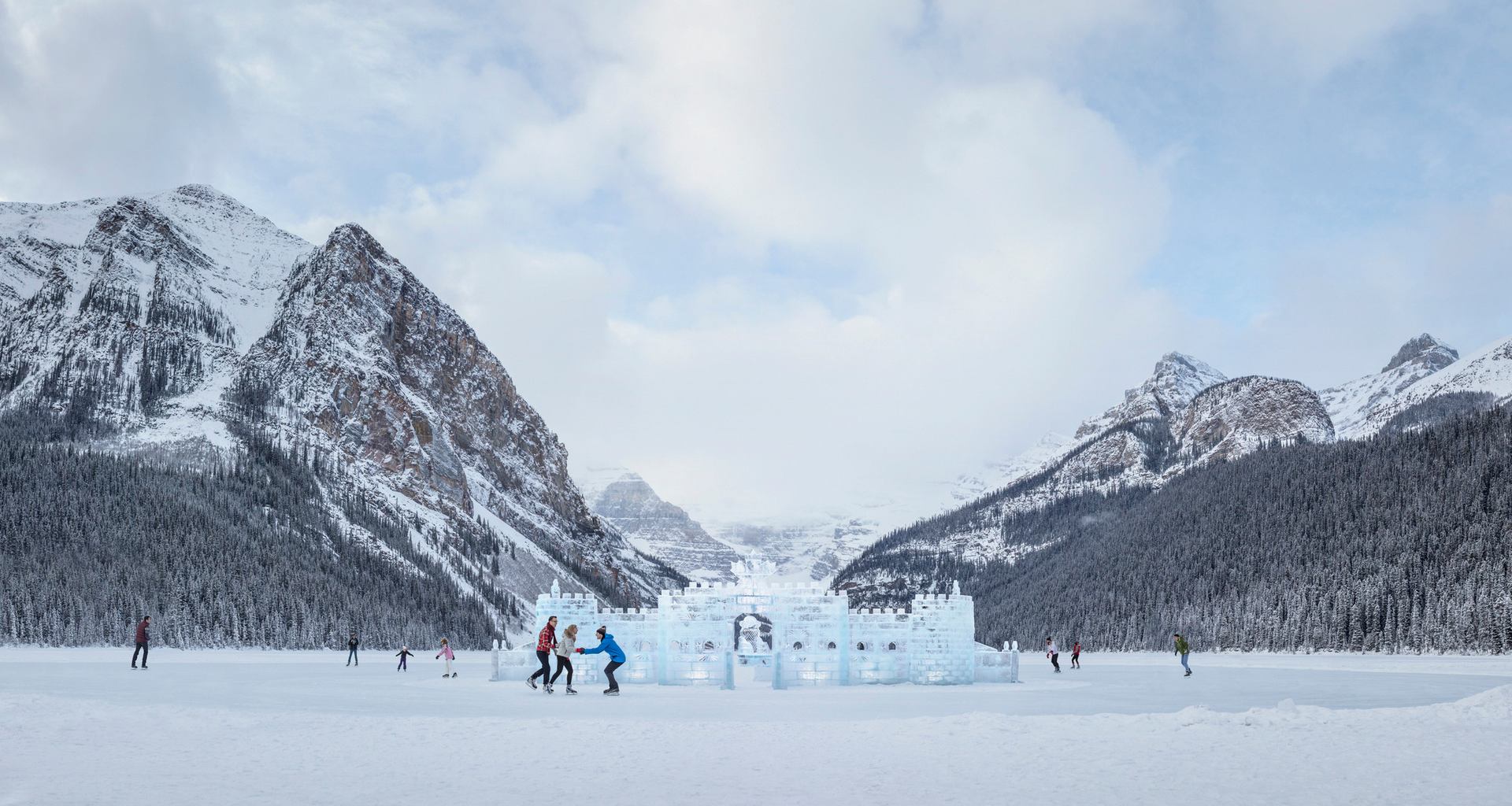 People ice skating around an ice castle, mountains in the background, on Lake Louise in Banff National Park.