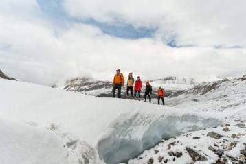 Group of four smiling as they follow a tour guide along a glacier walk in the snow covered mountains.