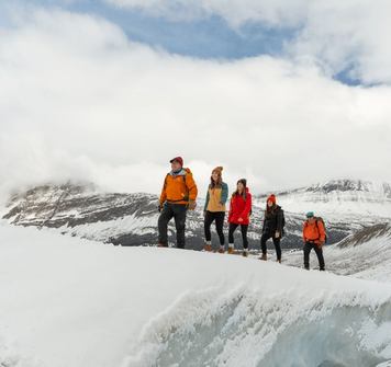 Group of four smiling as they follow a tour guide along a glacier walk in the snow covered mountains.