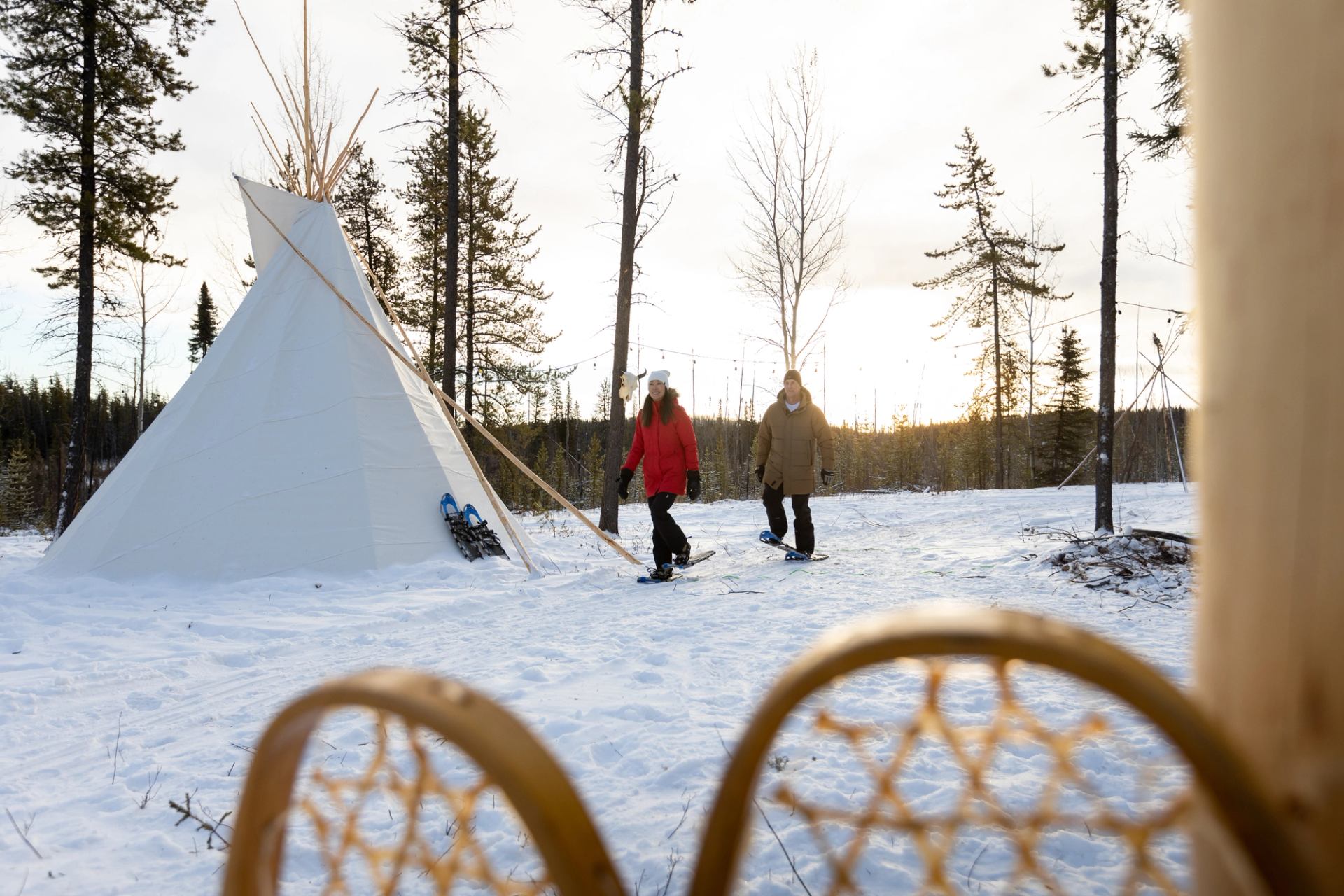 A couple snowshoeing by a tipi at the Aurora Borealis Indigenous Village