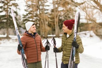 Two people with cross country skis on a snowy trail near a stand of trees.