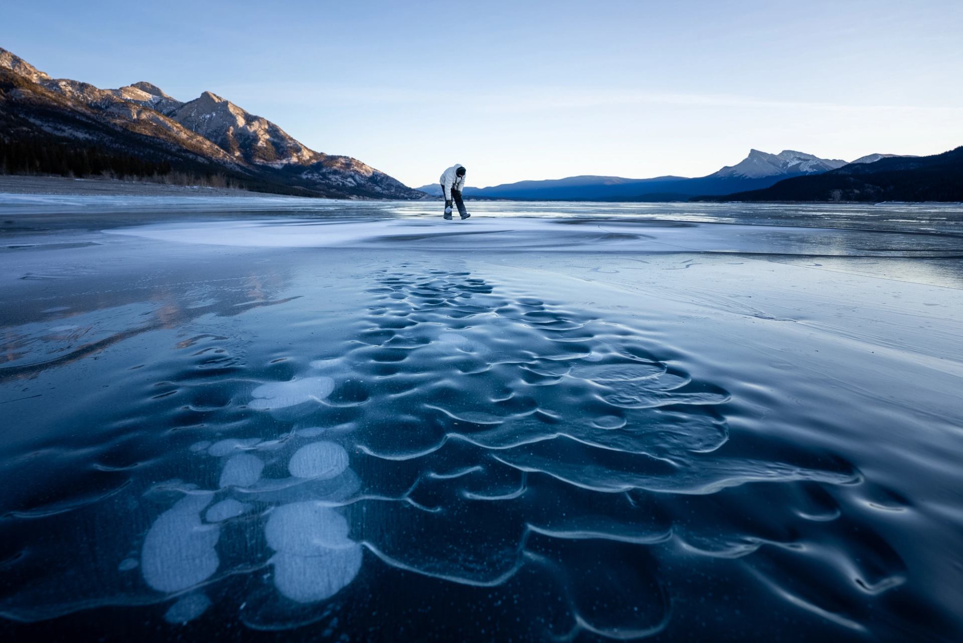 Frozen ripples on the surface of Abraham Lake while in the distance artist David Popa creates art on the frozen surface.