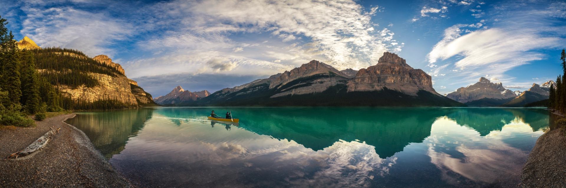 Two paddlers in a yellow canoe with a reflection of the mountains at Maligne Lake in Jasper National Park.