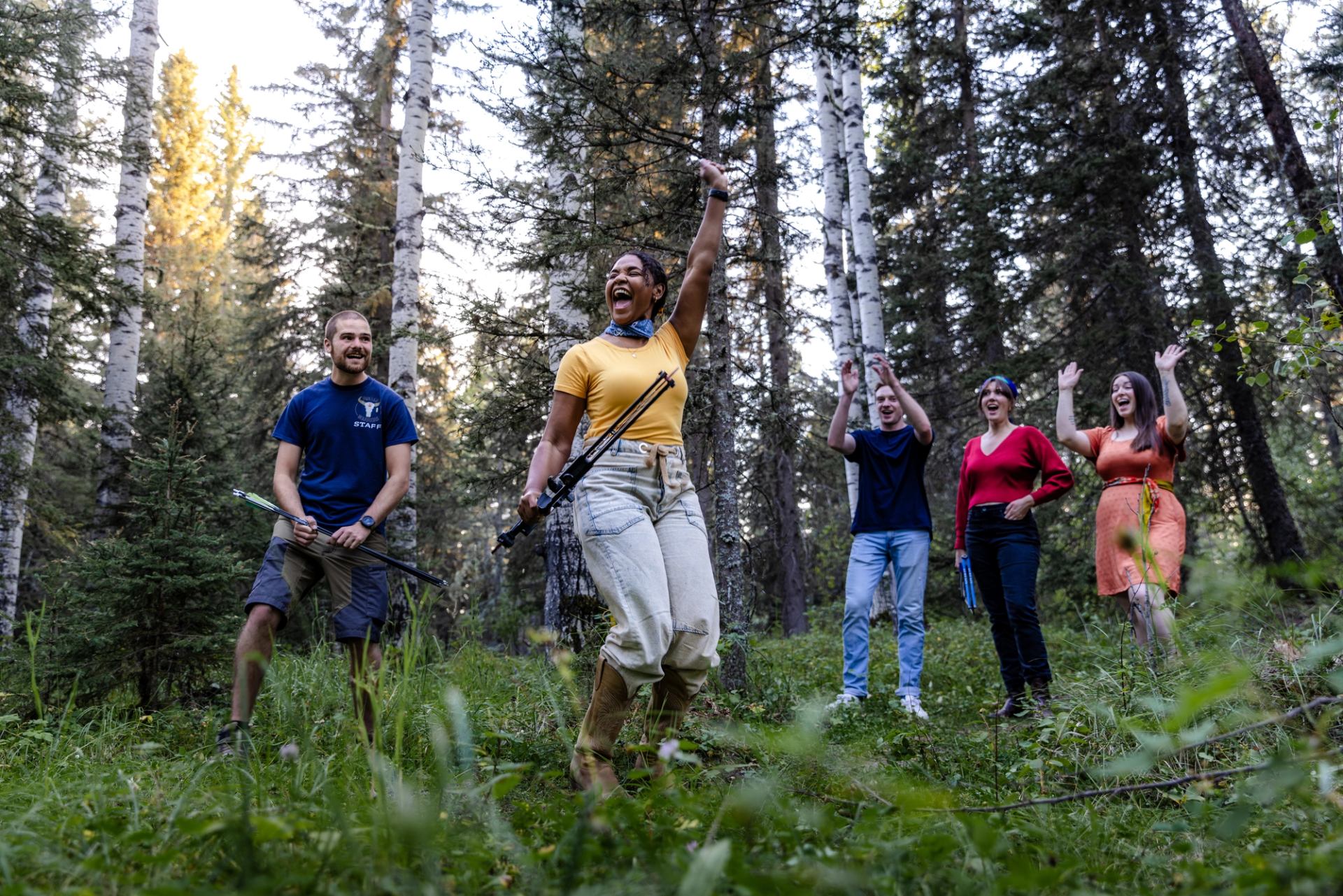 A woman and her friends cheer while trying archery in a forest.
