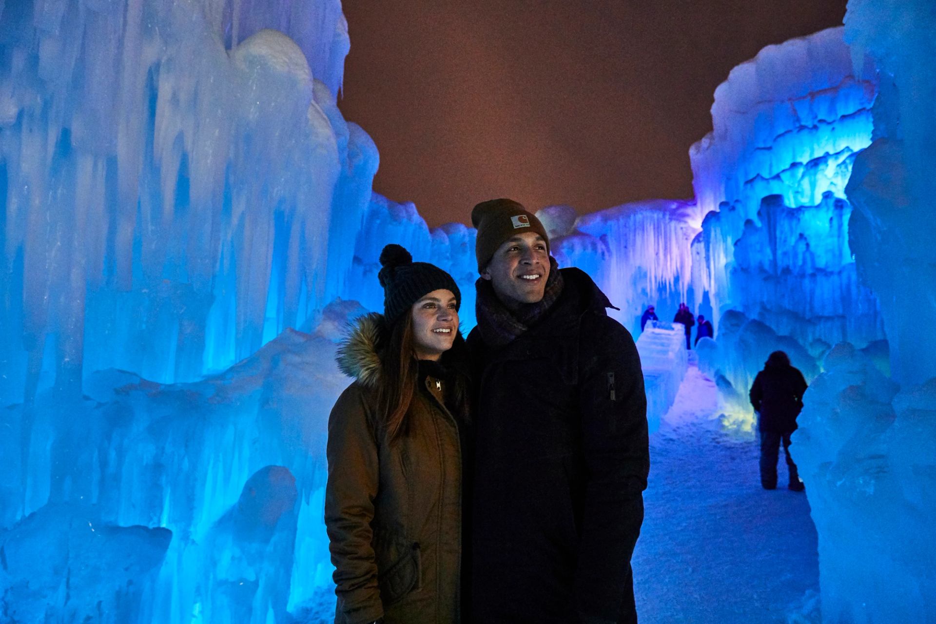 A couple walks at night through a sereies of ice sculptures.