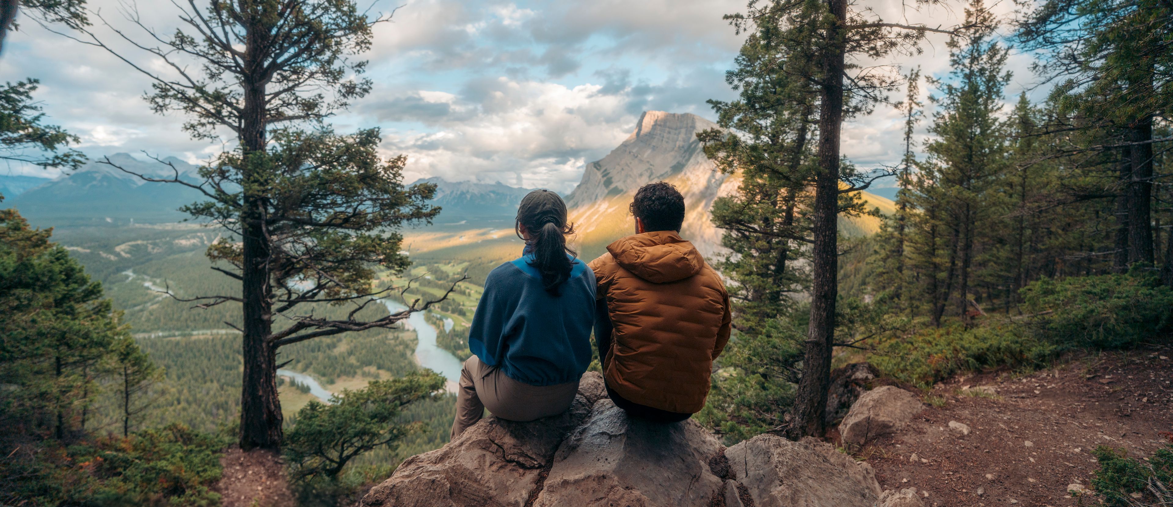 Two hikers overlook to the view from Tunnel Mountain while sitting on a rock.