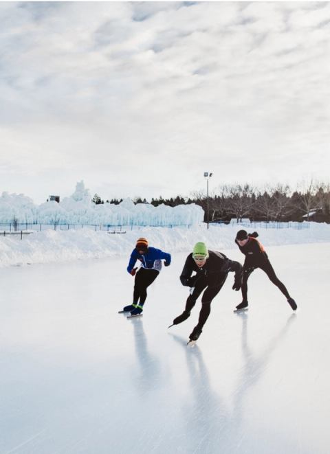 Three speed skaters gliding on an outdoor skating track.