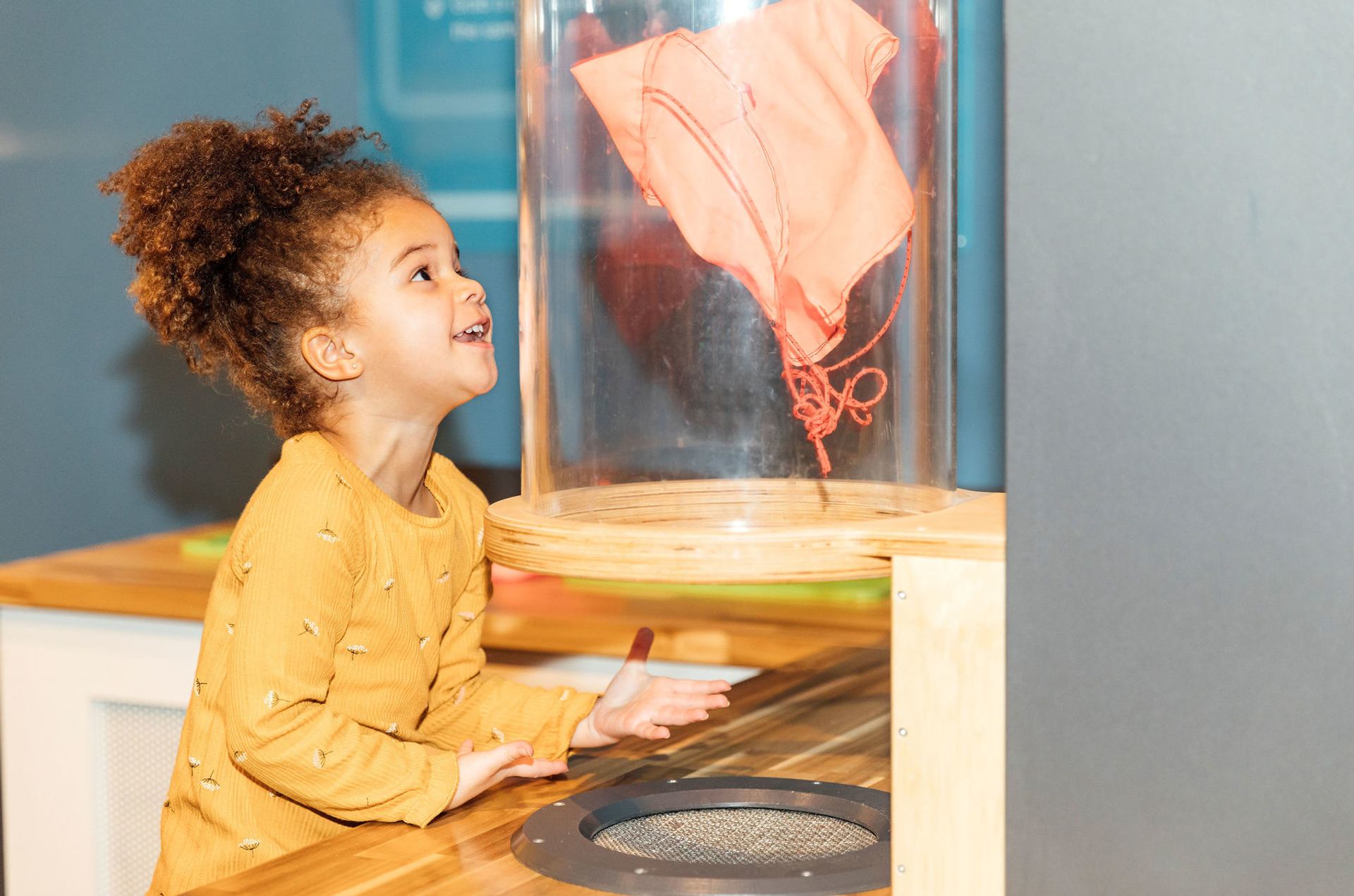 A young girl smiles and watches an object floating in a wind tunnel at the TELUS World of Science.