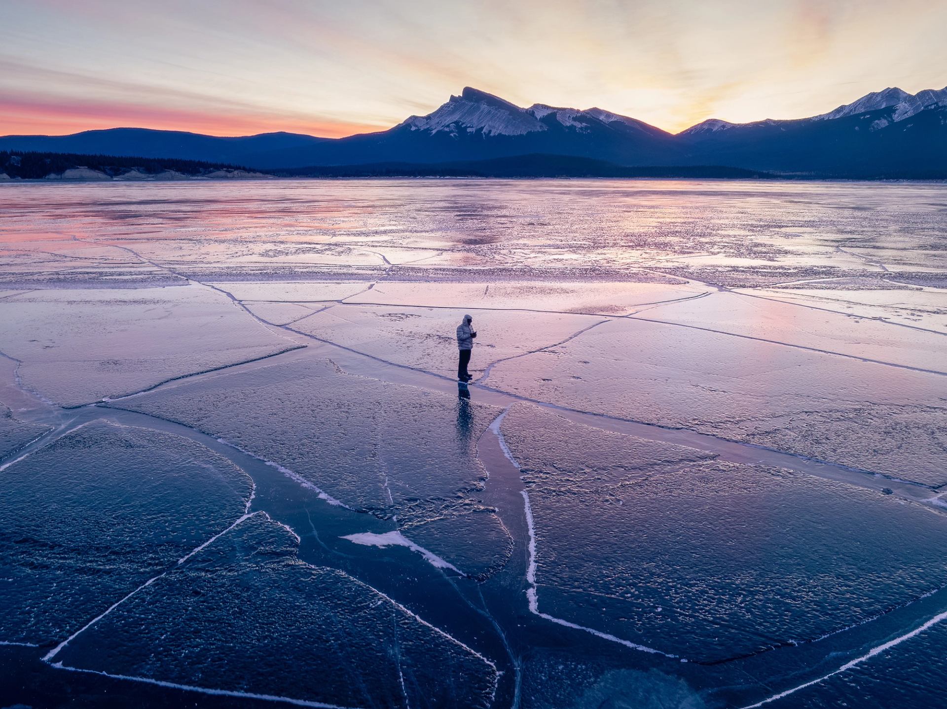 David Popa stands among cracked and refrozen ice on Abraham Lake at sunset with mountains in the distance.
