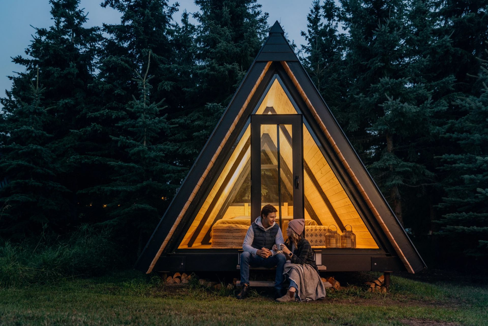 A man and a woman sit on the steps of Pine Creek Retreat comfort cabins at dusk, located near Smoky Lake.
