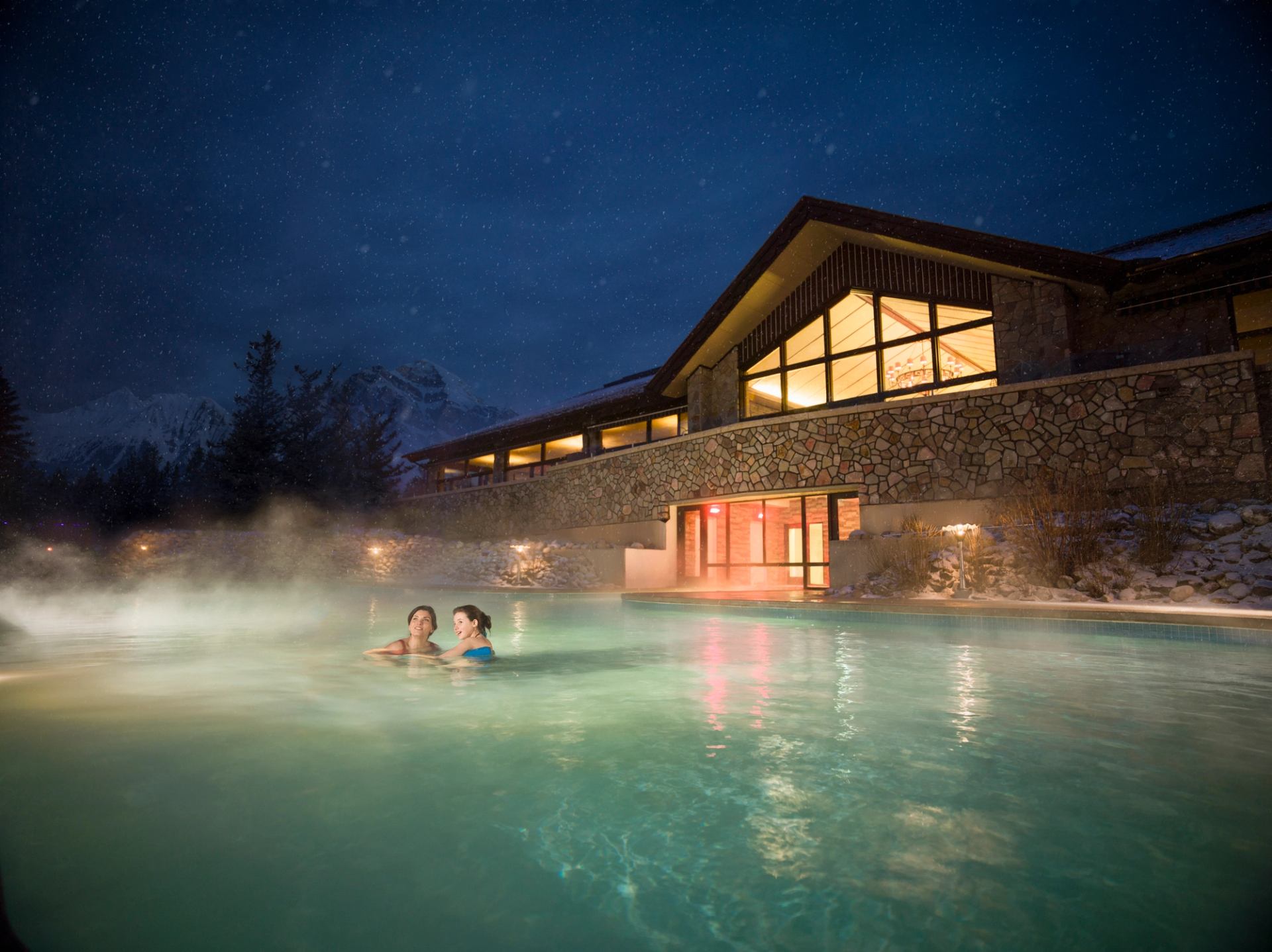 Family swimming in the outdoor pool at night at the Fairmont Jasper Park Lodge