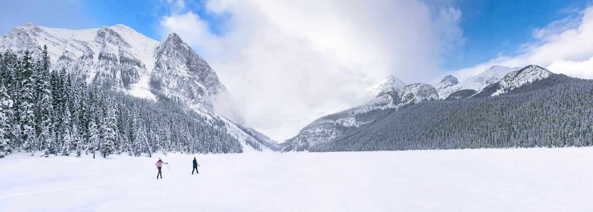 Two cross country skiers cross Lake Louise, surrounded with epic mountain views, in Banff National Park