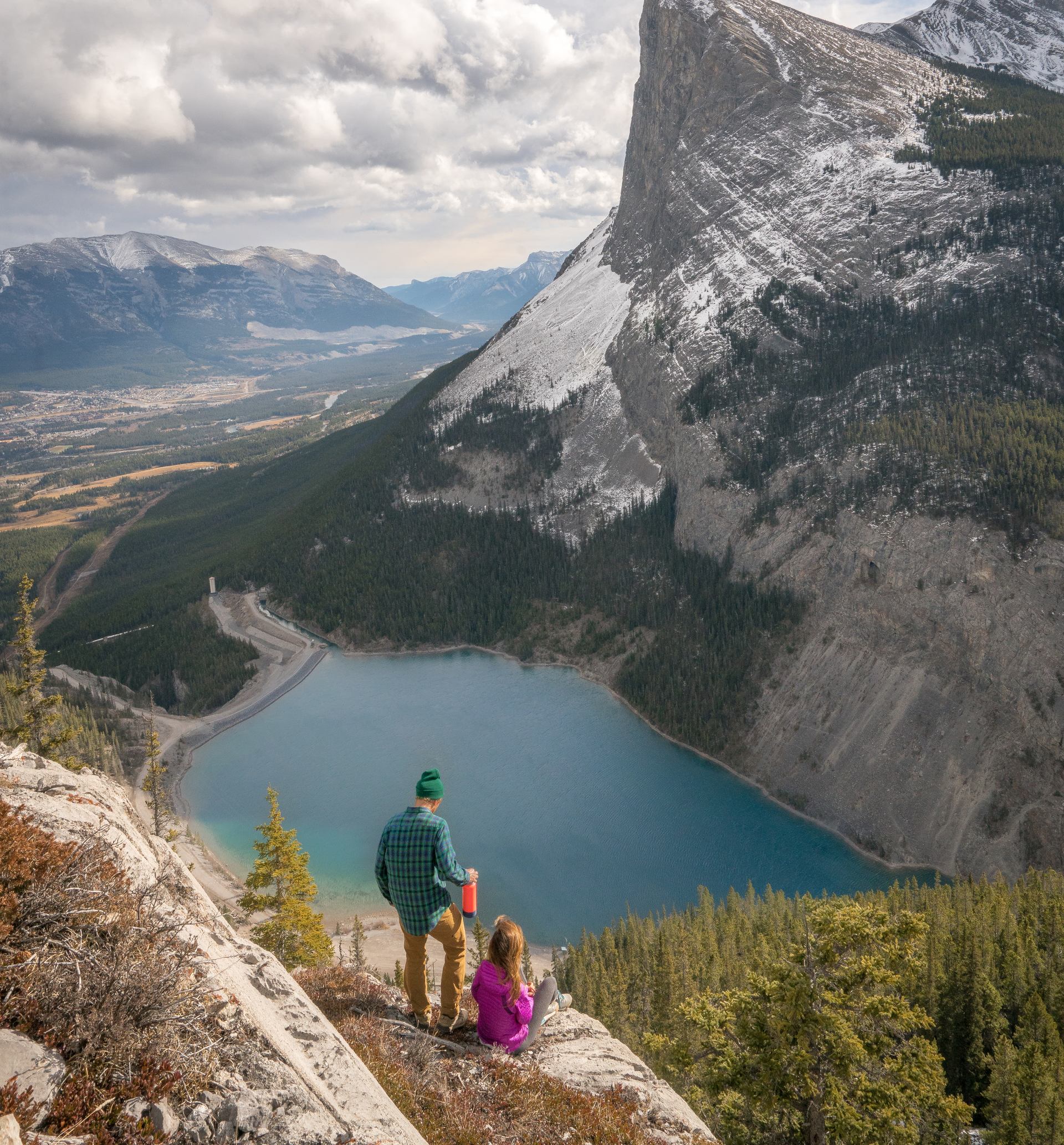 Two hikers pause on a cliffside overlooking a mountain lake.