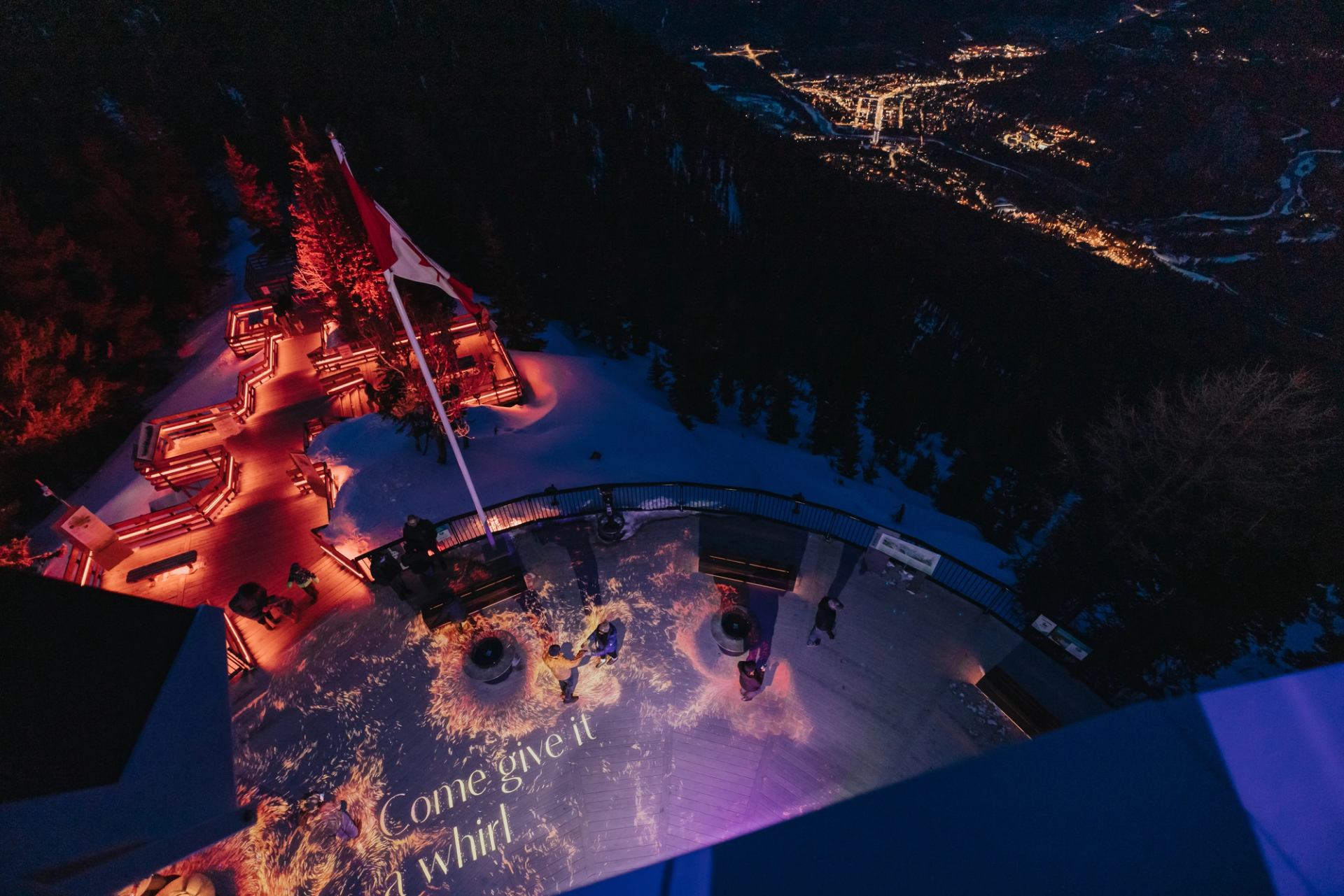 An aerial view of people enjoying the light show in the evening at Pursuit's Nightrise Experience at the Banff Gondola.