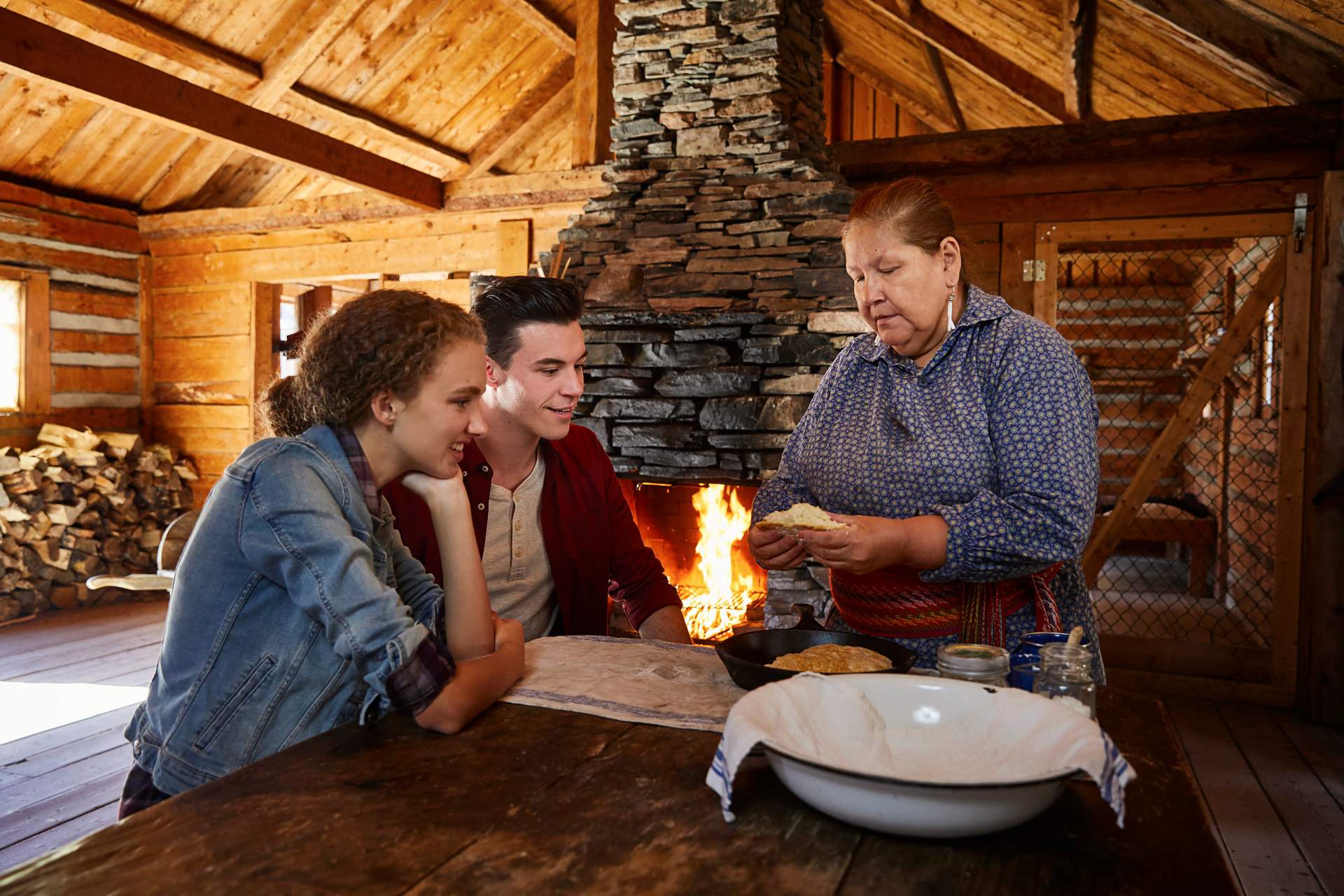 A woman shows a couple how to make bread in an old cabin.