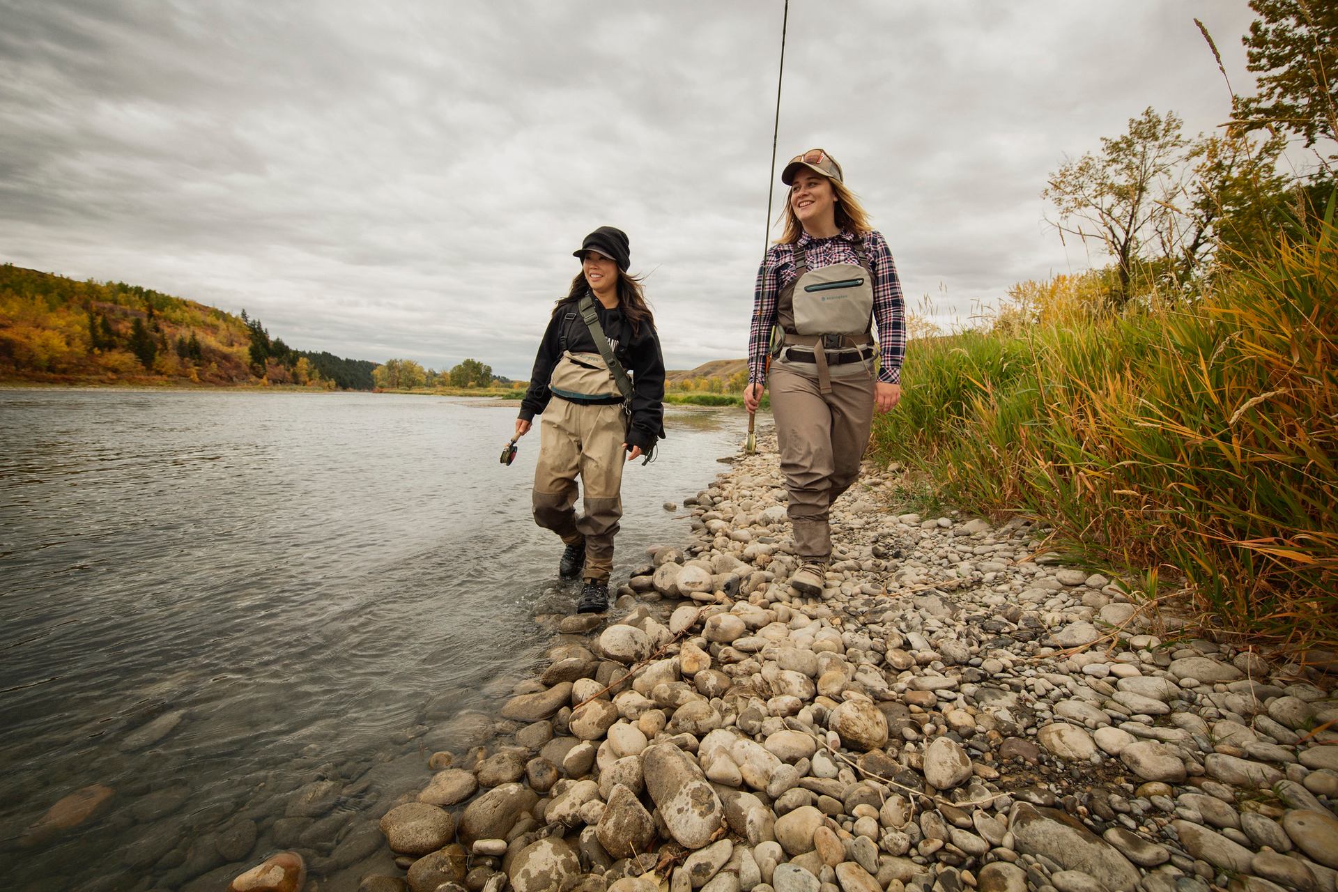 Two women walk along the river while out fly fishing.