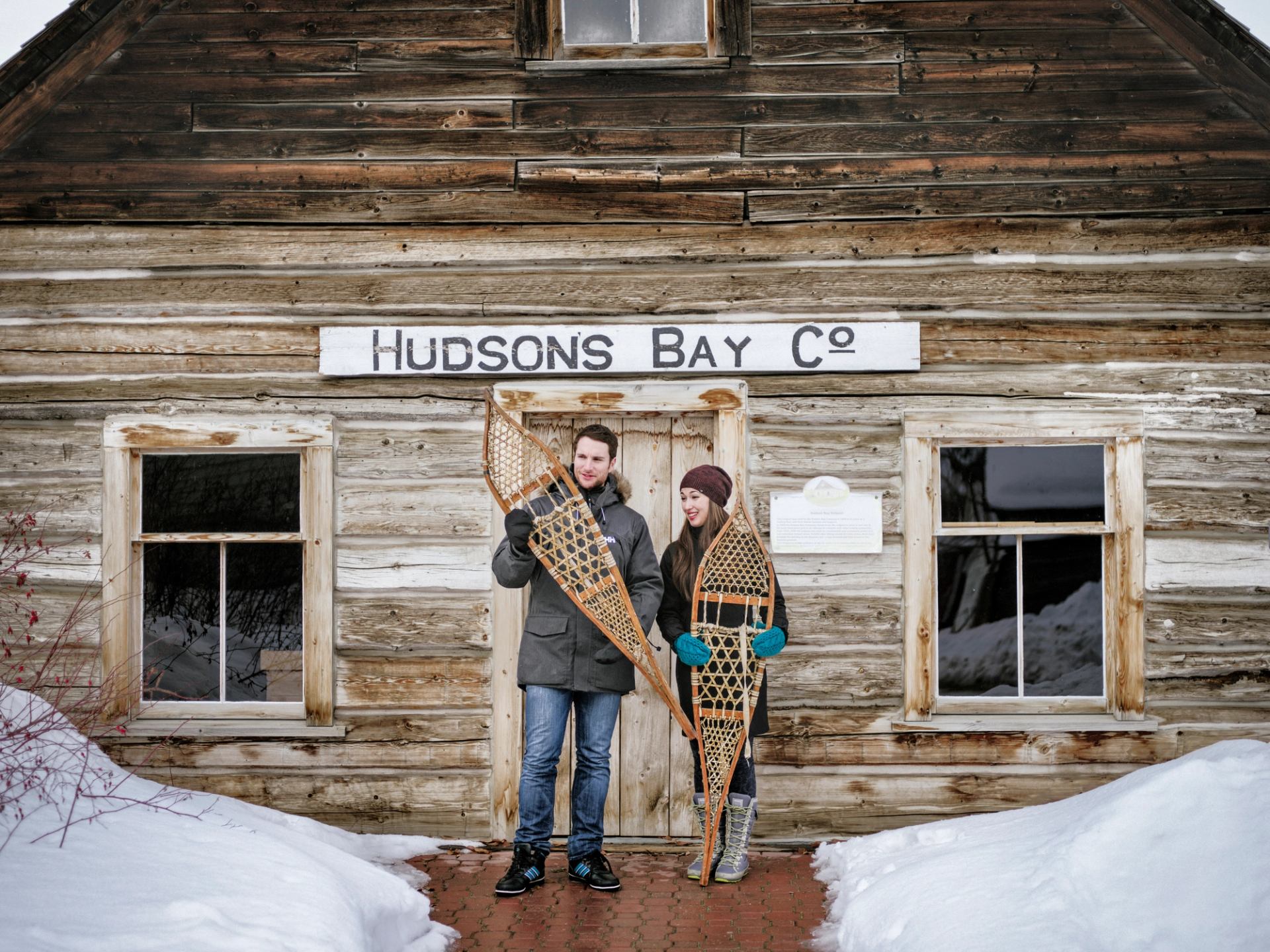 Couple with old fashioned snowshoes in front of the historic Hudson's Bay Building at the Grande Prairie Museum and Heritage Village