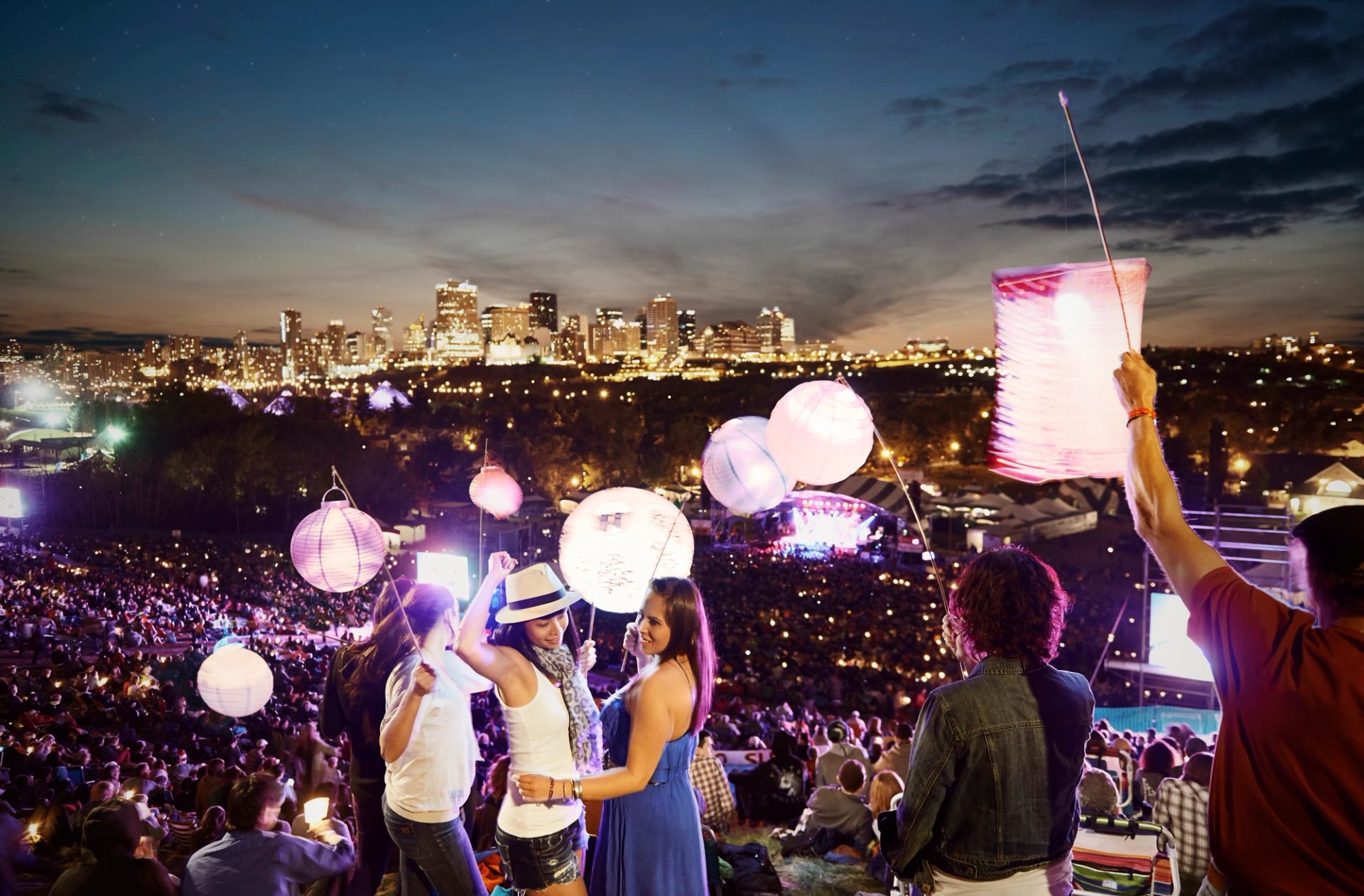 Crowd of people holding lanterns while listening to music at an outdoor music festival at night.