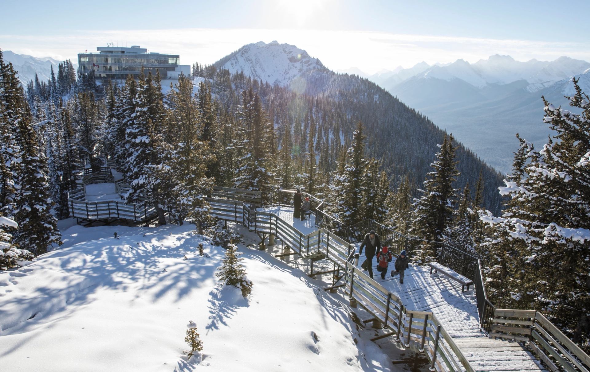 Visitors walk the snow-dusted boardwalk near the summit of Sulphur mountain with the interpretive centre in the background.