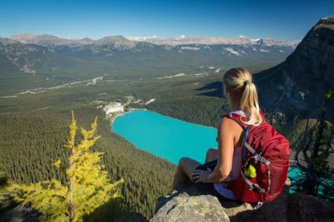 Hiker sitting on a rock ledge at Little Beehive with views of turquoise Lake Louise in Banff National Park.