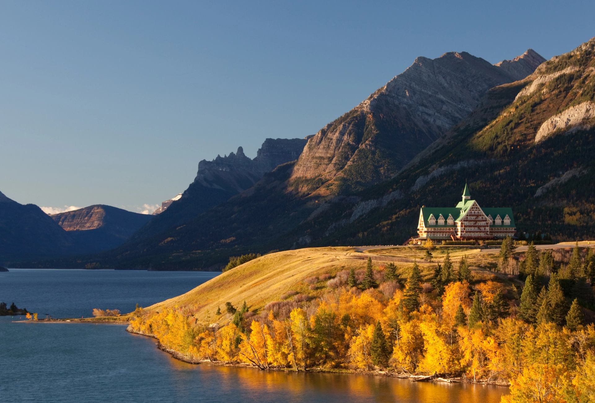 Historic hotel on a hill above a lake with a mountain view in the background.