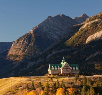 Historic hotel on a hill above a lake with a mountain view in the background.