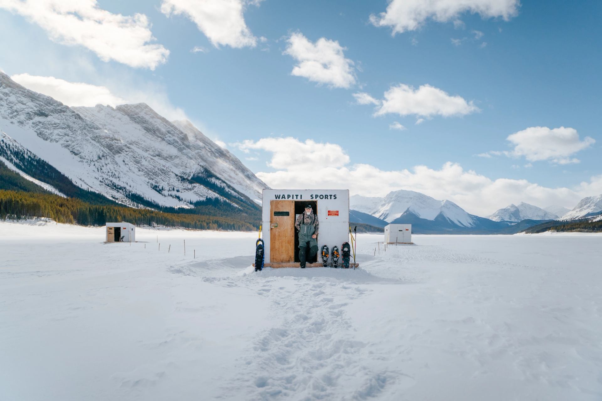 A man stands in the door frame of a hut in the middle of a frozen lake near Canmore in Kananaskis Country.