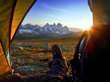 Point of view of a person looking out of a tent onto a mountain view while they are camping in the wildlands while the sun sets