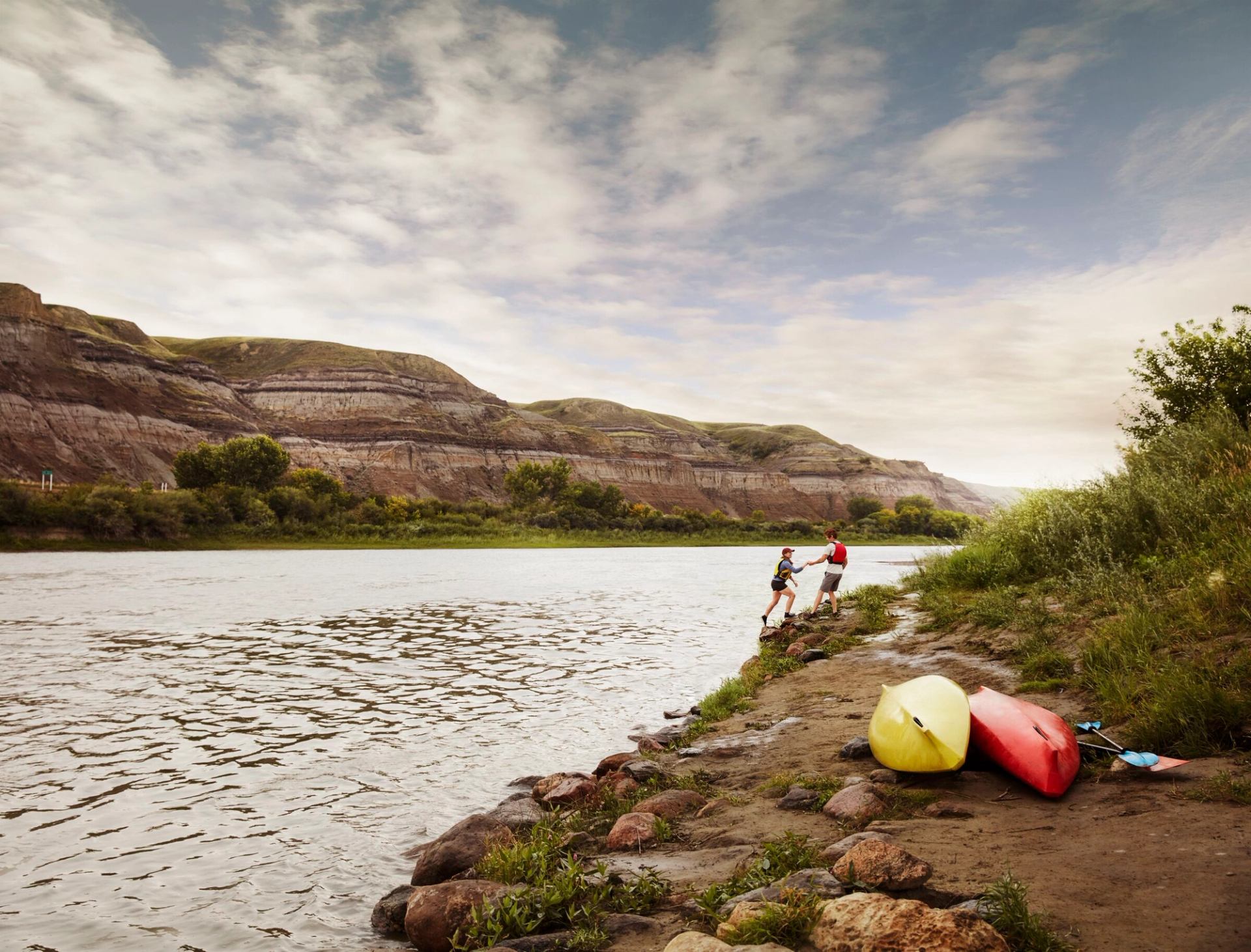 A couple play near the waters edge with their kayaks on the hillside.
