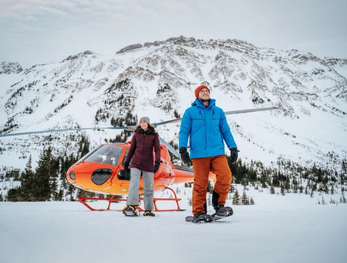 Couple on a mountain with a helicopter behind them
