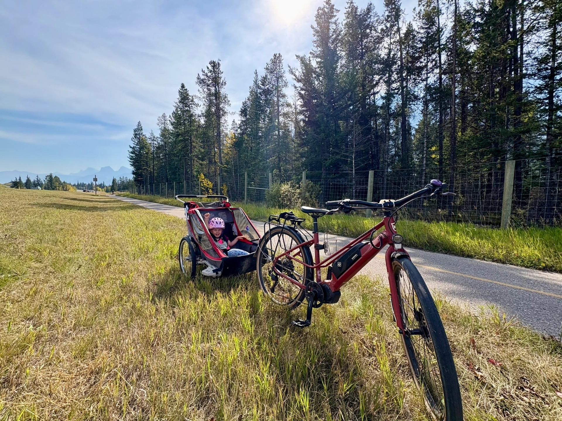 A young child cheers in the back of a bike trailer hooked up to an e-bike next to the Rocky Mountain Legacy Trail in Banff National Park.