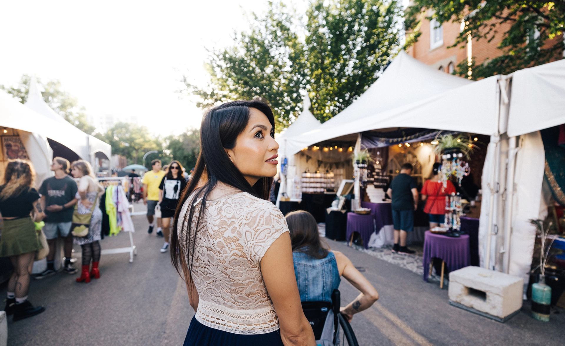 A woman walks through the artisan market at Edmonton International Fringe Festival, with booths on either side of her.