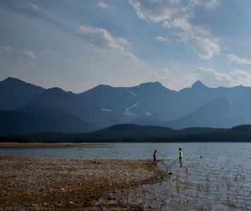 People swimming in Lower Kananaskis Lake surrounded by mountains in Kananaskis Country.