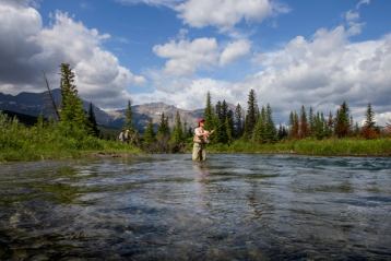 Women fly fishing with mountains behind her