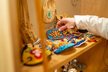 Someone picks up a Beaded Orange Flower Barrette from a shelf full of other beadwork arts and crafts as well as ceremonial and medicine bags.