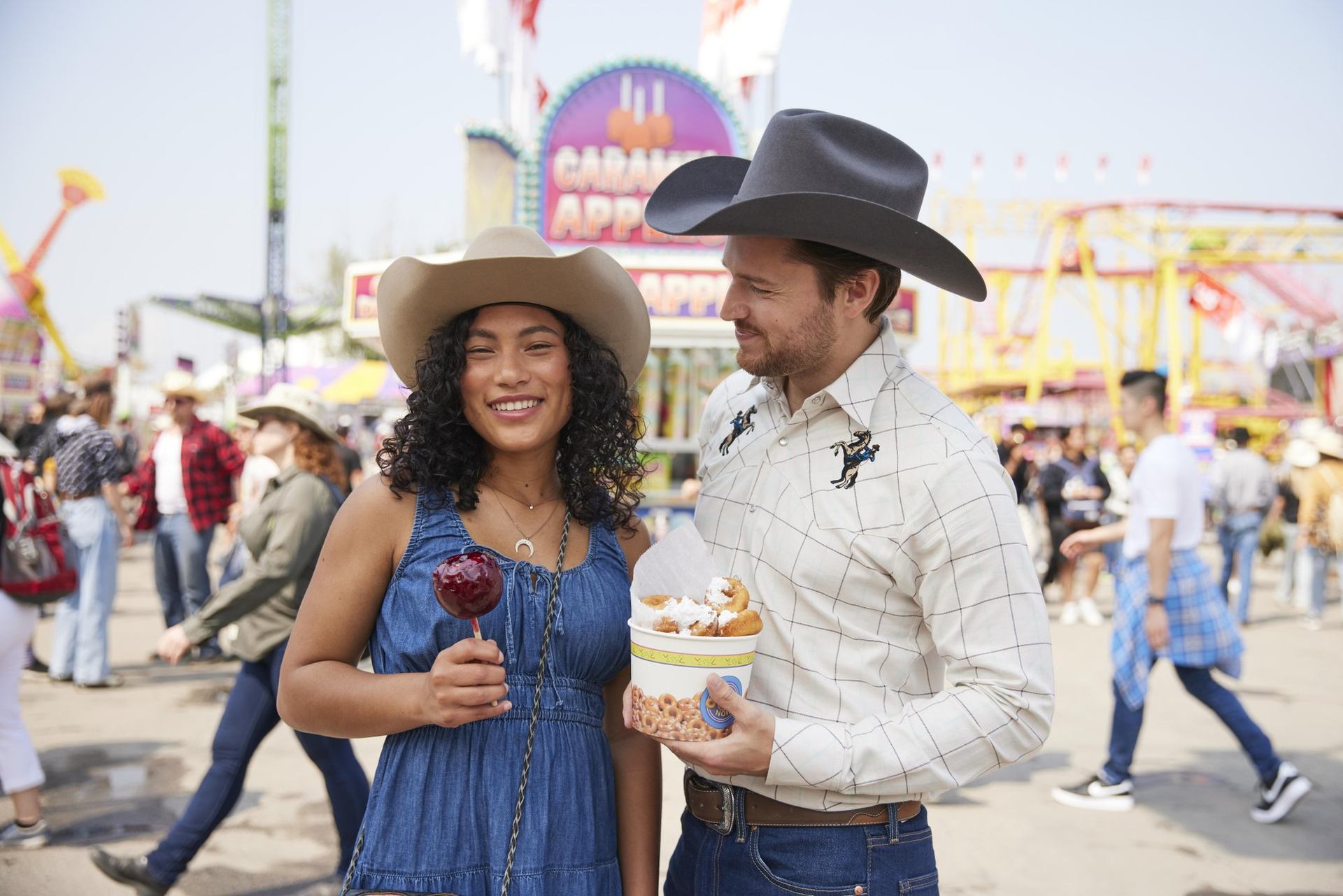 Two Stampede-goers with a candy apple and mini doughnuts.