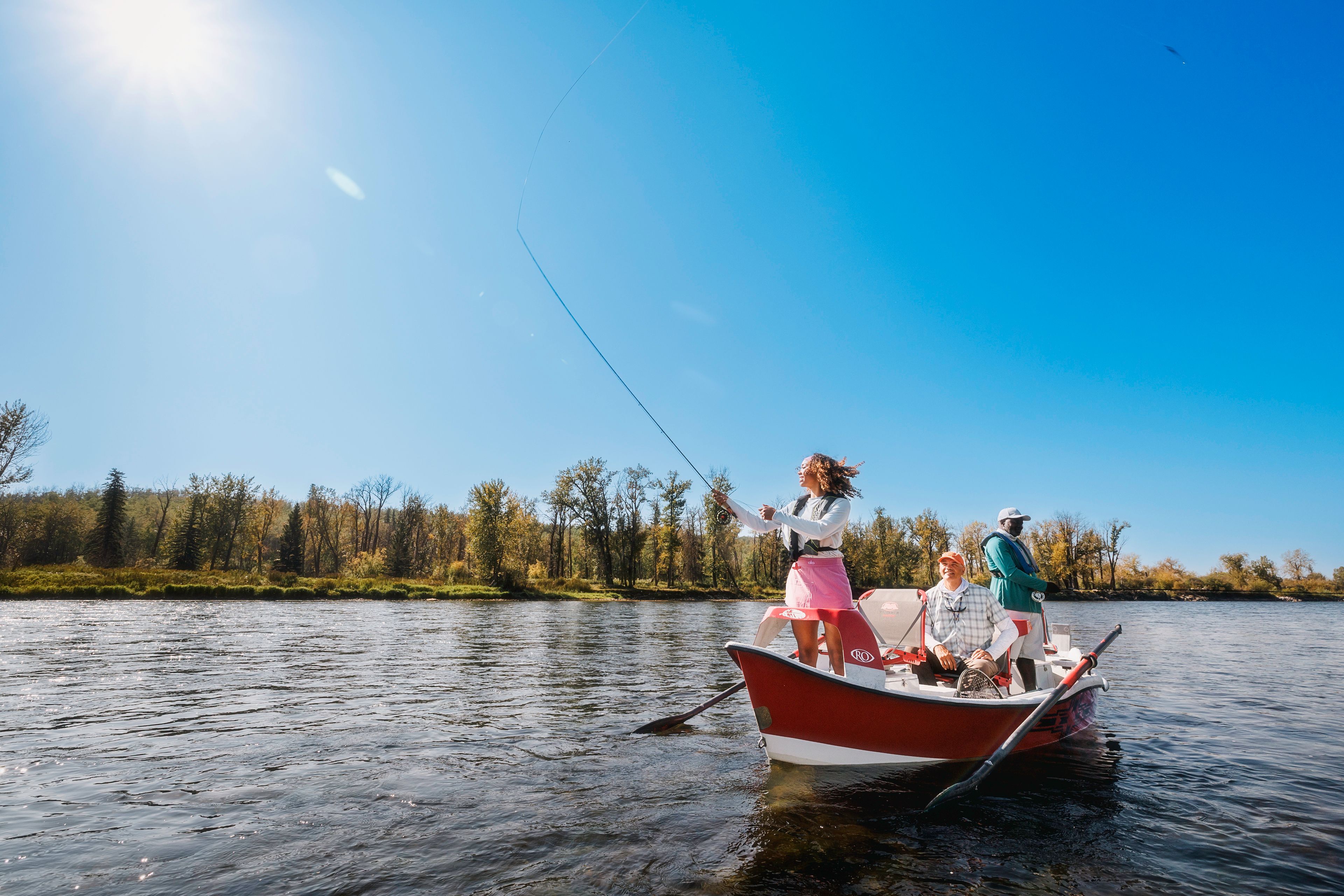 A teen girl casts a fly rod from the bow of a drift boat while her father and their guide look on during a fishing trip on the Bow River south of Calgary, Alberta.
