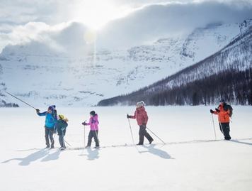 A family gliding across a lake on a guided cross country ski tour with the sun shining over mountains in the background.
