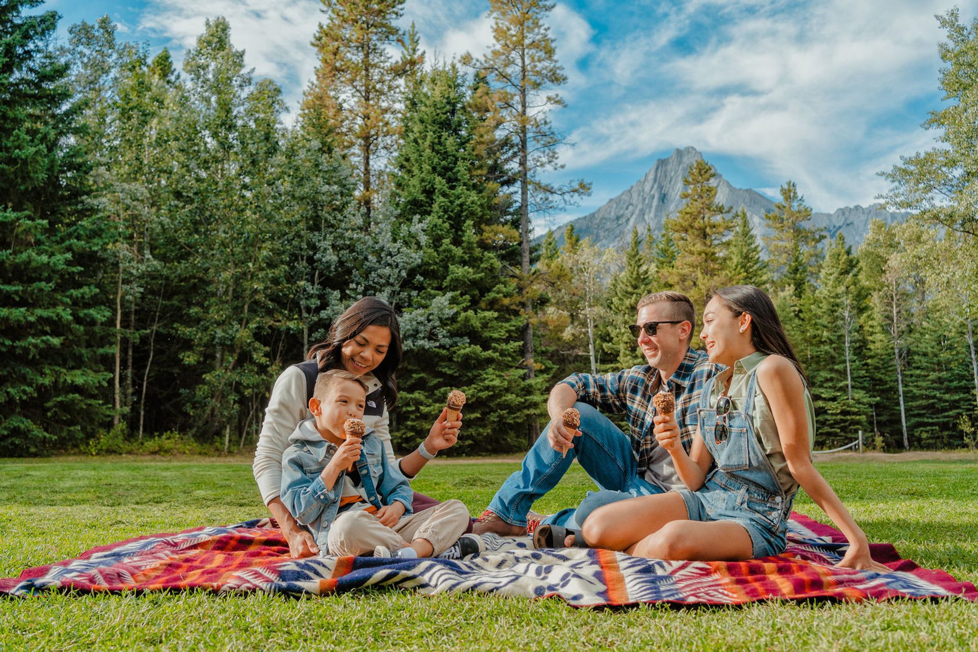 People eat ice cream on a lawn with trees and mountains in the background.