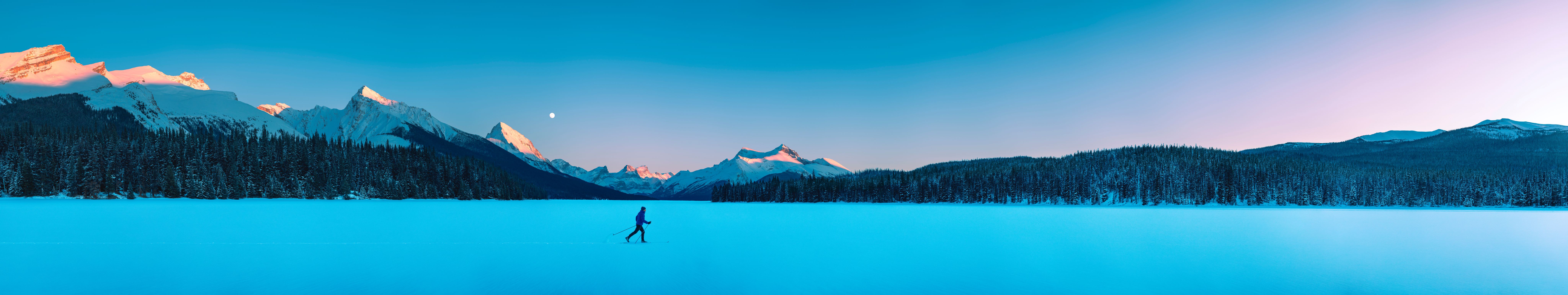 A cross country skier skis across Jasper National Park's Maligne Lake with mountains in the distance.