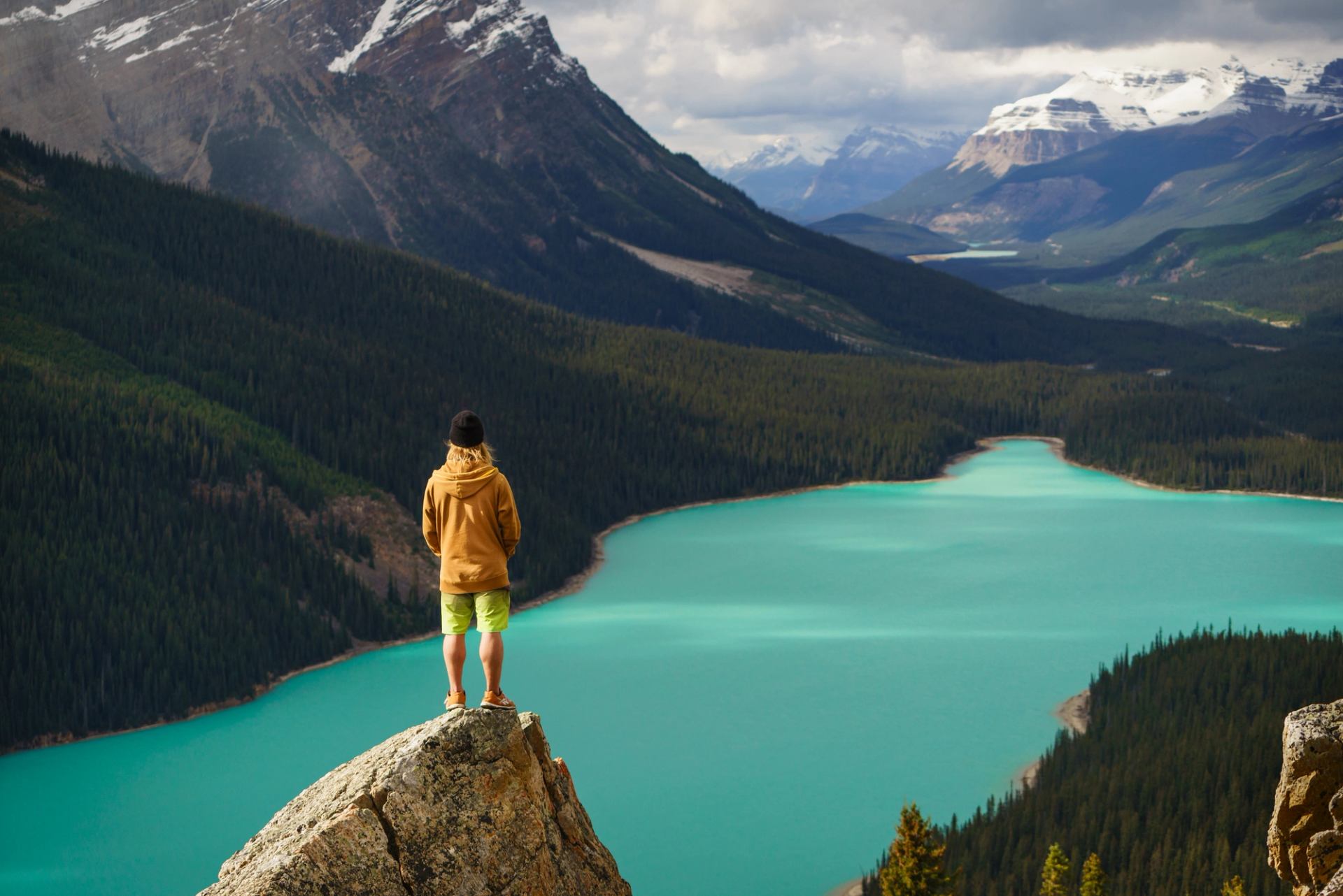 Hiker standing on the tip of a rock at the top of their hike overlooking a lake and mountain view.