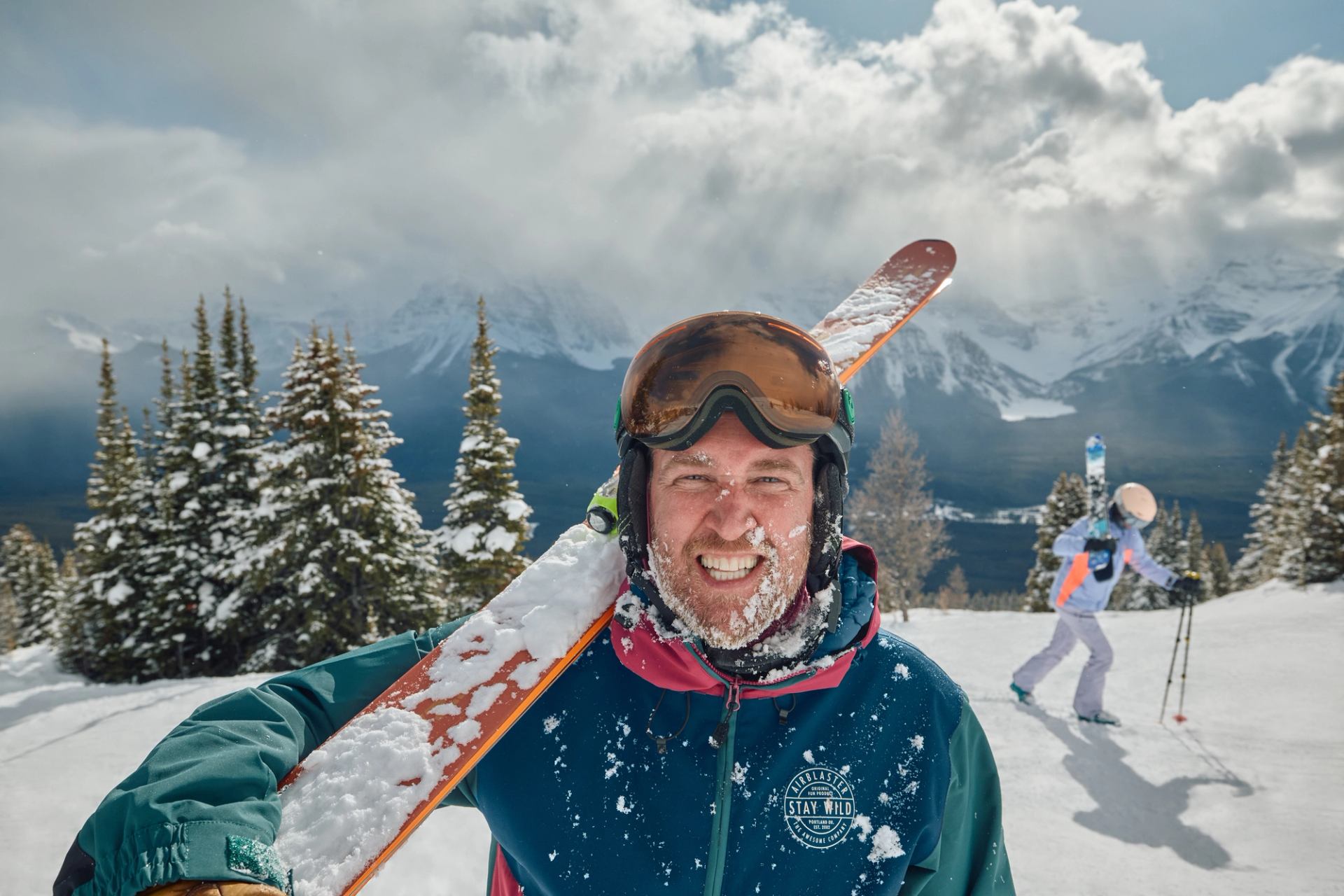 Person carrying skis with snowy mountain backdrop.