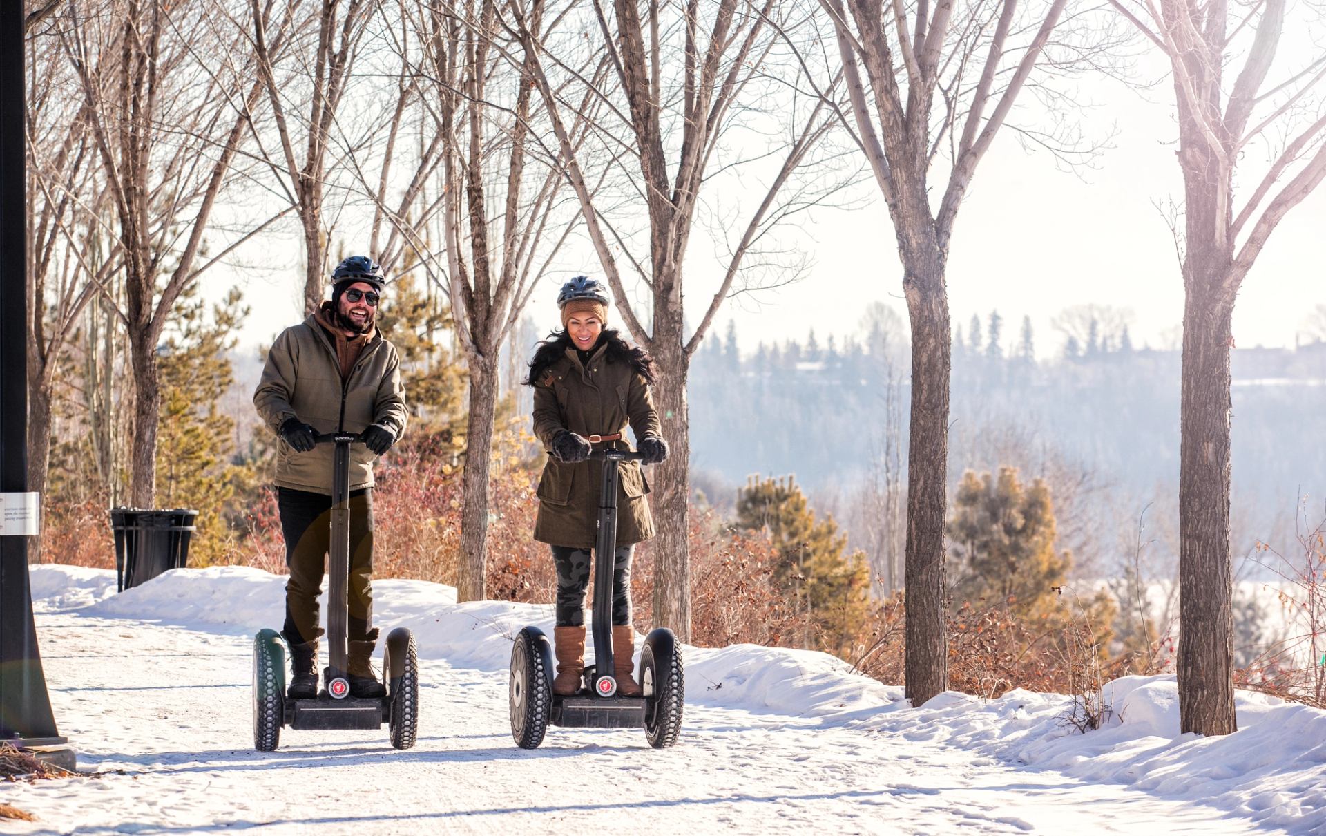 A couple ride along a snowy path on segways.