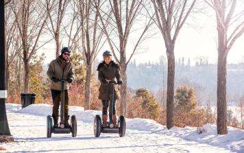 A couple riding a Segway down a wintery path, through Louise McKinney Park in Edmonton