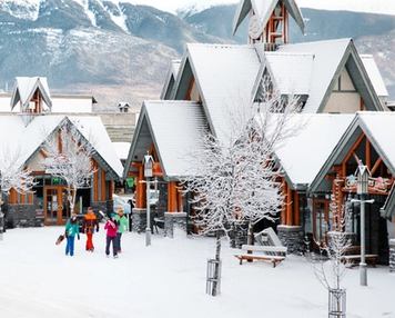 Skiers and snowboarders walking in downtown Jasper, with buildings and shops in the background.