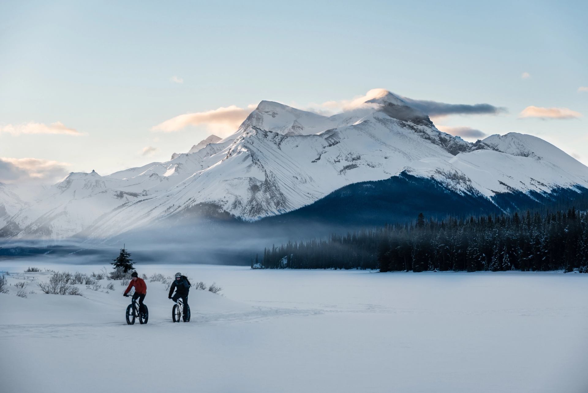 Two people fat biking on a frozen Maligne Lake on winter day in Jasper National Park.