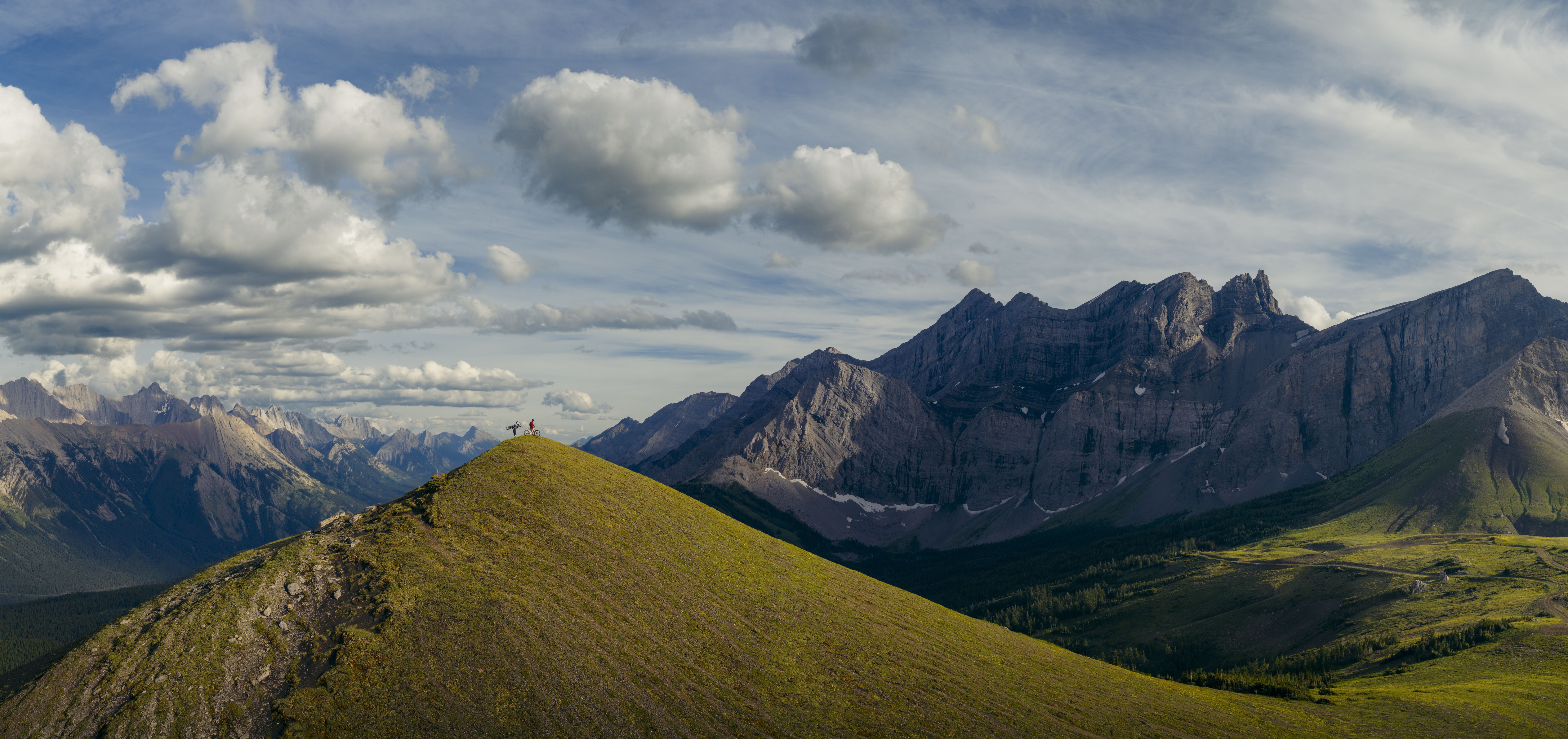 Two bikers pause on the peak to enjoy the view of the surrounding mountains.