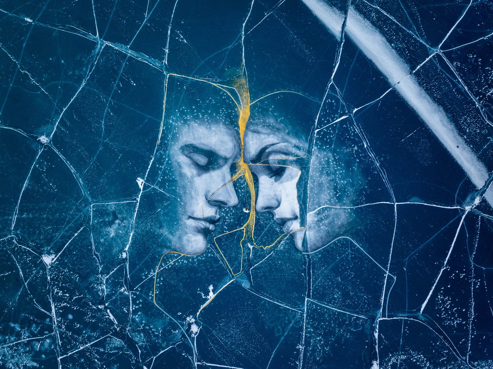 Charcoal art of a male and female face with their foreheads nearly touching are divided by a gold-coloured crack in the ice they’re painted on.