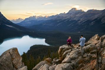 A couple take pictures while sitting on the rocks overlooking Peyto Lake in Banff National Park.